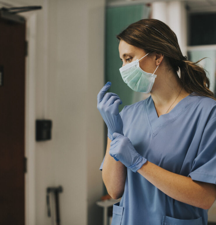 Female nurse with a mask putting on gloves
